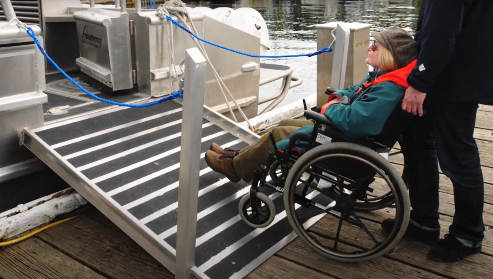 Eine Person im Rollstuhl steigt über eine barrierefreie Rampe in ein Boot ein.