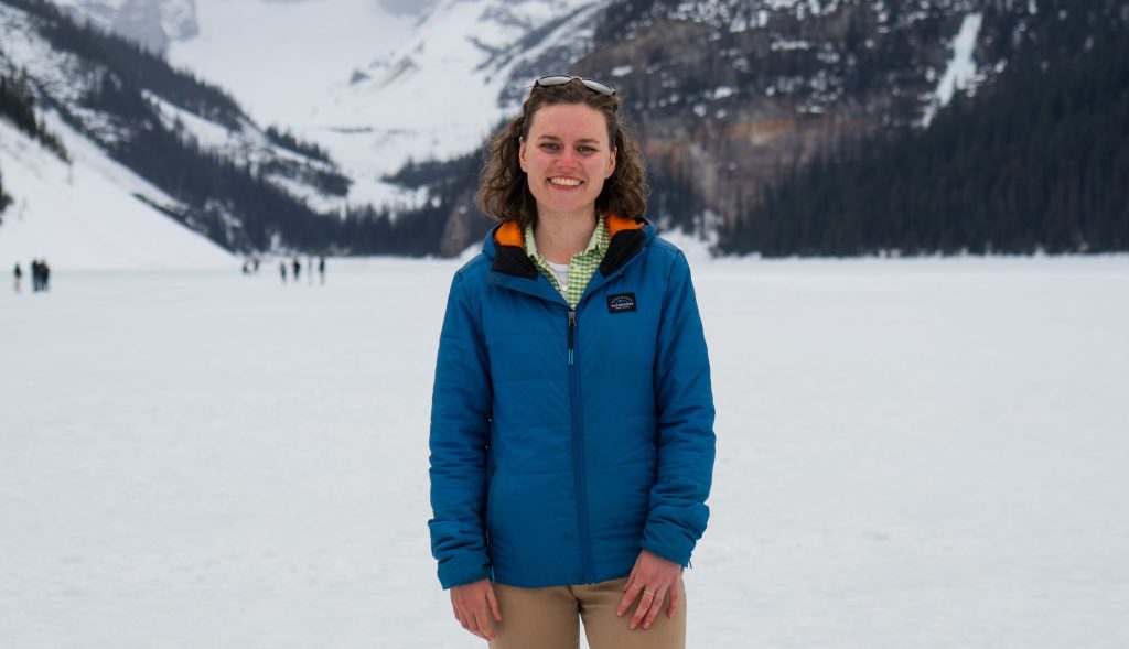 Alice Daish in einer blauen Jacke lächelt vor einer verschneiten Berglandschaft.