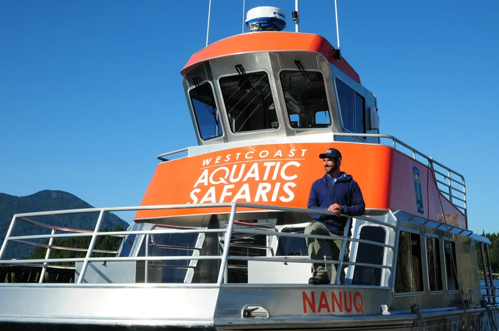 Man standing on a Westcoast Aquatic Safaris boat under a clear blue sky.