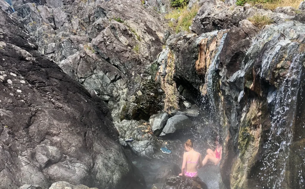 People soaking beside a rocky waterfall.